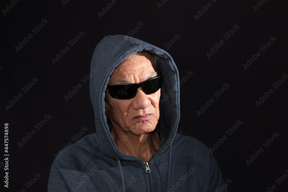 Older man wearing a dark hoodie and shades against a black background Older man wearing a dark hoodie and shades against a black background