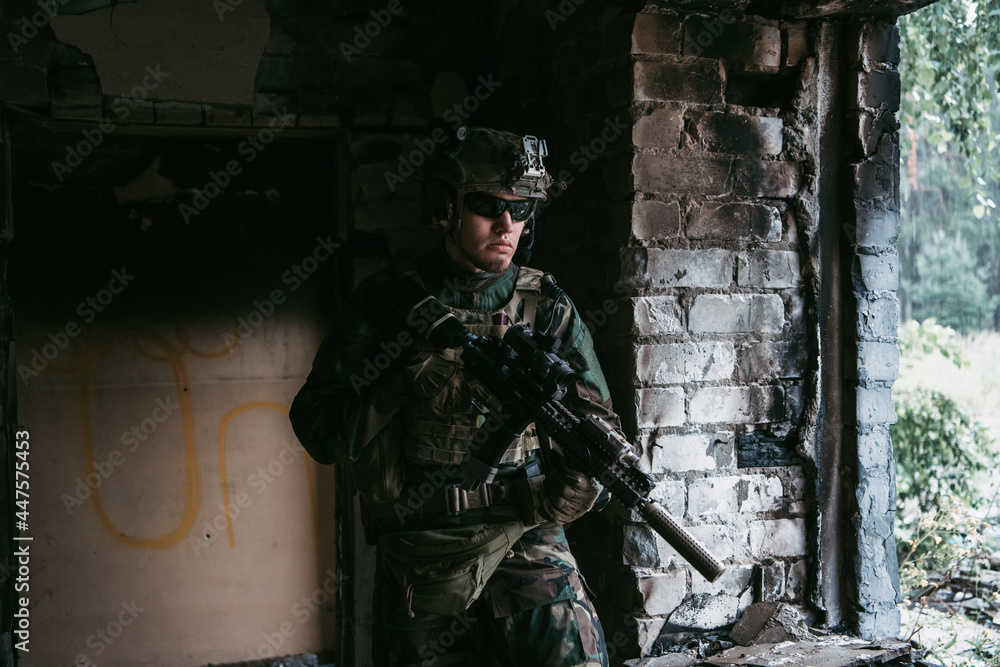 Military man with assault rifle standing inside building, he is ready for combat Military man with assault rifle standing inside building, he is ready for combat
