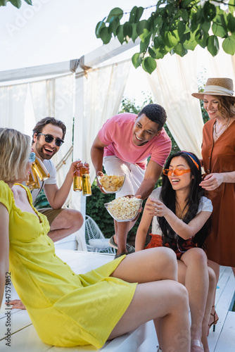 excited multiethnic friends with beer and snacks having fun during summer party