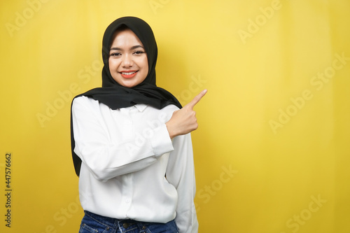Beautiful young asian muslim woman with hands pointing empty space presenting something, smiling confident, enthusiastic, cheerful, looking at camera, isolated on yellow background