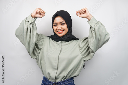 Beautiful young asian muslim woman confident and smiling, with clenched fist, punching, sign for spirit, fighting, victory sign, isolated on gray background