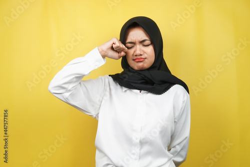 Beautiful young muslim woman crying, hands wiping tears, isolated on yellow background © MunirSr