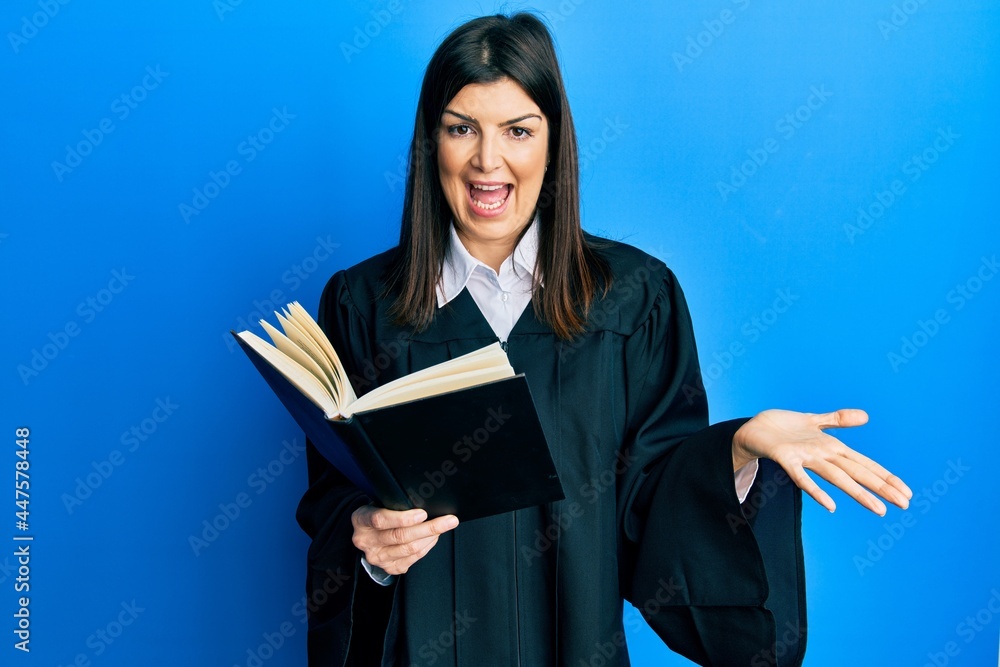 Young hispanic woman wearing judge uniform reading book celebrating achievement with happy smile and winner expression with raised hand Young hispanic woman wearing judge uniform reading book celebrating achievement with happy smile and winner expression with raised hand