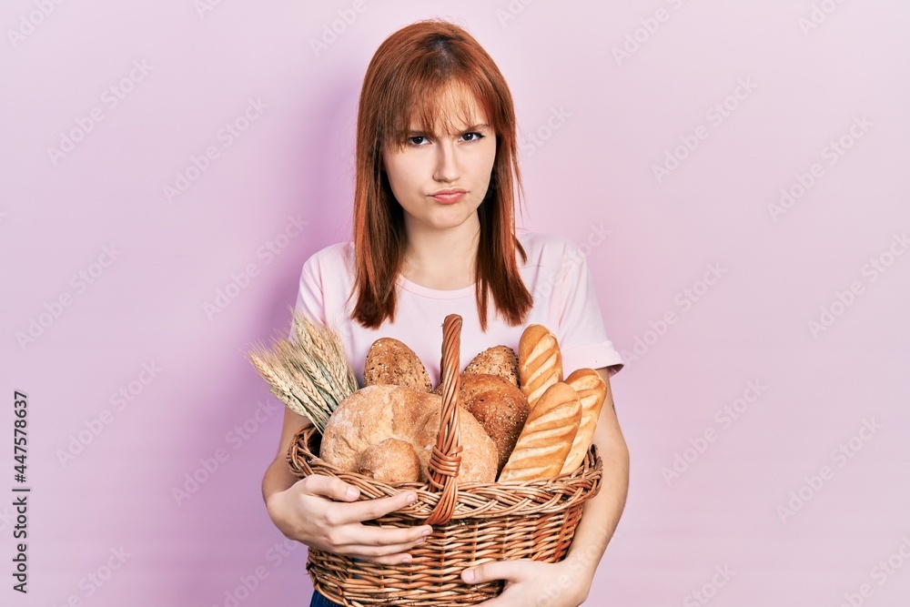 Redhead young woman holding wicker basket with bread skeptic and nervous, frowning upset because of problem. negative person. Redhead young woman holding wicker basket with bread skeptic and nervous, frowning upset because of problem. negative person.
