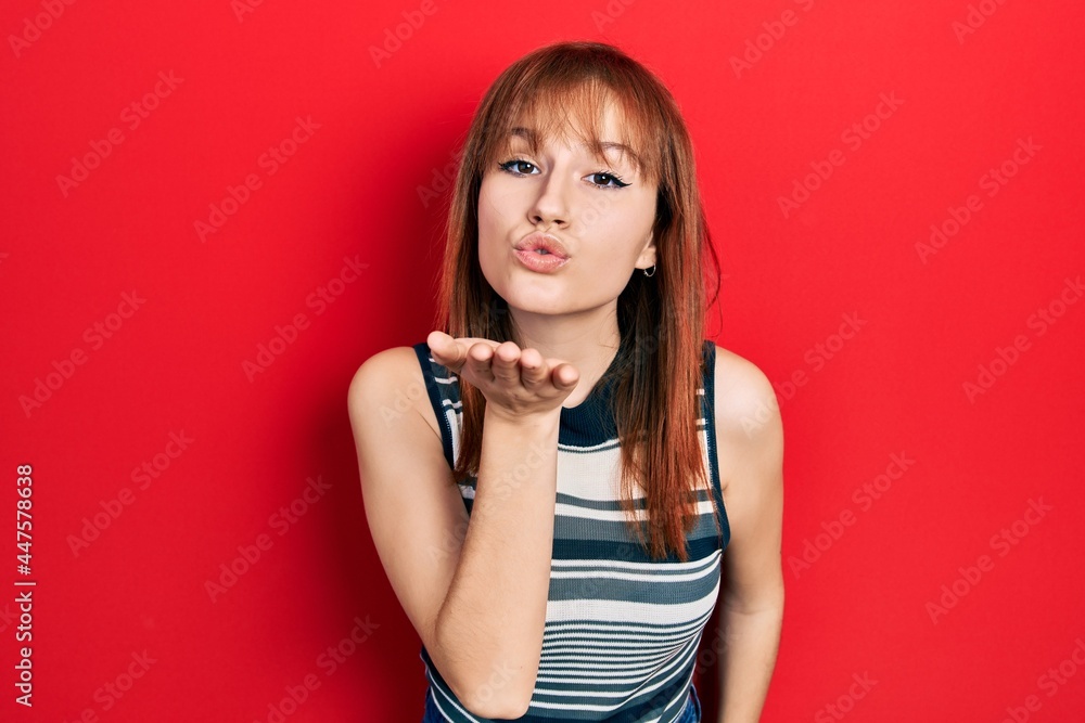 Redhead young woman wearing casual t shirt looking at the camera blowing a kiss with hand on air being lovely and sexy. love expression. Redhead young woman wearing casual t shirt looking at the camera blowing a kiss with hand on air being lovely and sexy. love expression.