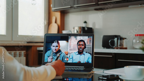 Close-up shot of Multiracial colleagues working home on quarantine by making common video call by computer. Black man sitting in the kitchen and writing.