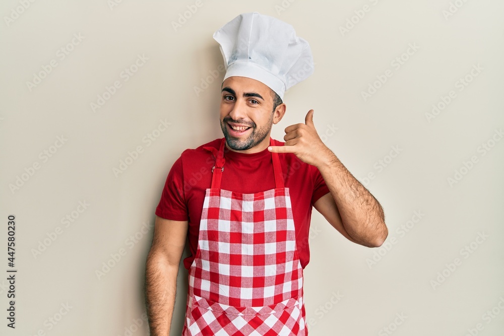 Young hispanic man wearing baker uniform smiling doing phone gesture with hand and fingers like talking on the telephone. communicating concepts. Young hispanic man wearing baker uniform smiling doing phone gesture with hand and fingers like talking on the telephone. communicating concepts.