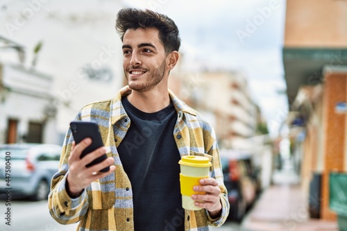 Handsome hispanic man smiling happy and confident at the city using smartphone