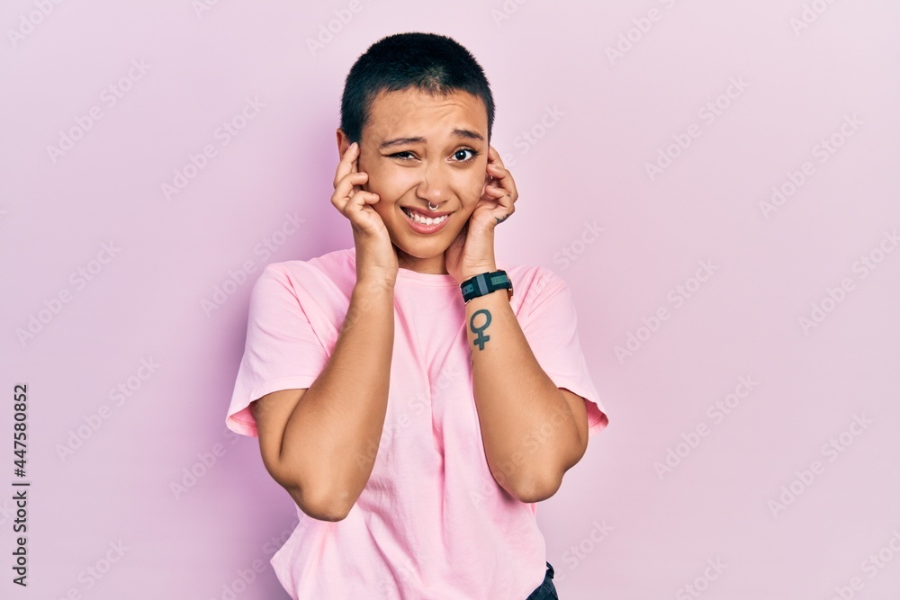 Beautiful hispanic woman with short hair wearing casual pink t shirt covering ears with fingers with annoyed expression for the noise of loud music. deaf concept. Beautiful hispanic woman with short hair wearing casual pink t shirt covering ears with fingers with annoyed expression for the noise of loud music. deaf concept.