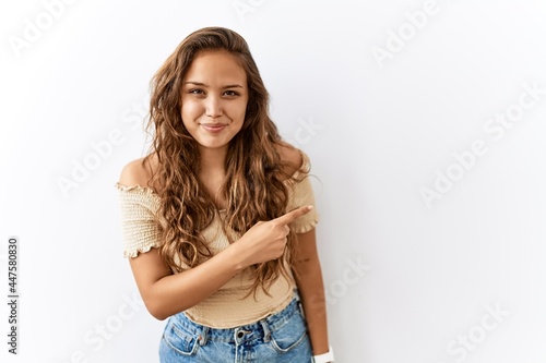 Beautiful hispanic woman standing over isolated while background cheerful with a smile of face pointing with hand and finger up to the side with happy and natural expression on face