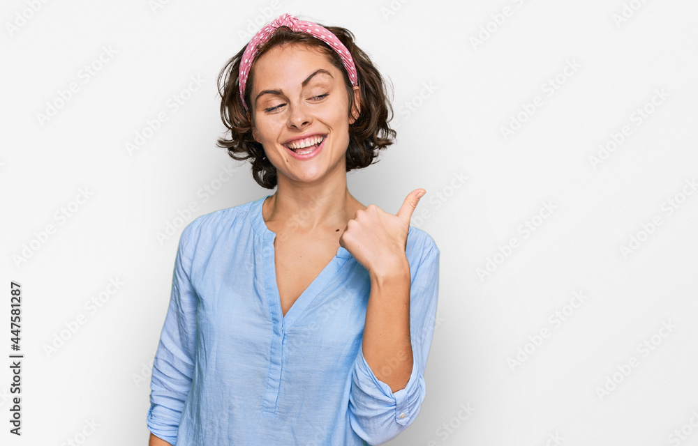 Young hispanic woman wearing casual clothes smiling with happy face looking and pointing to the side with thumb up.