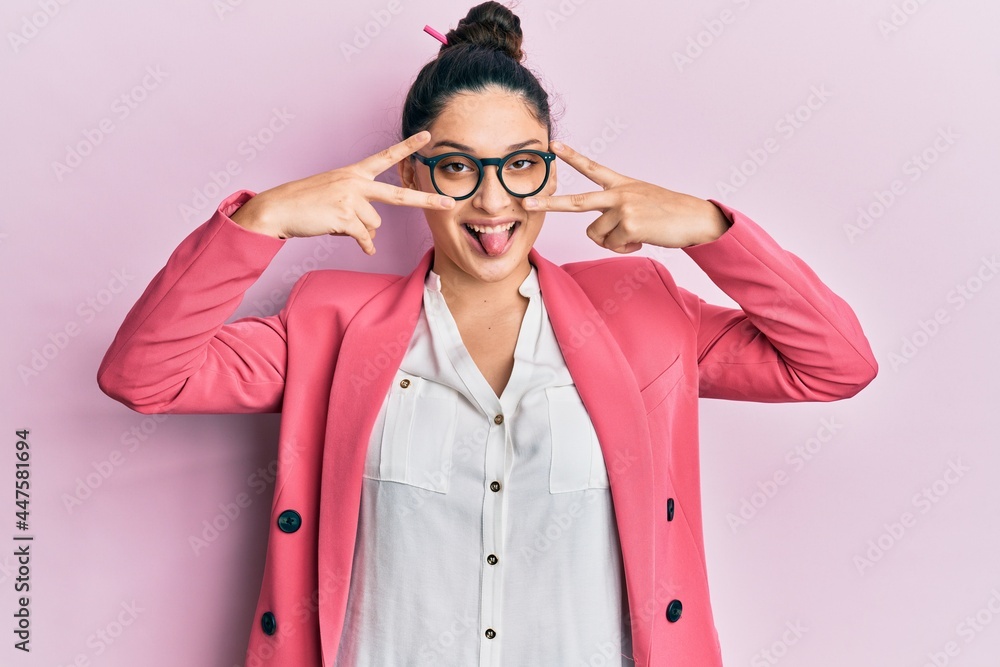 Beautiful middle eastern woman wearing business jacket and glasses doing peace symbol with fingers over face, smiling cheerful showing victory Beautiful middle eastern woman wearing business jacket and glasses doing peace symbol with fingers over face, smiling cheerful showing victory