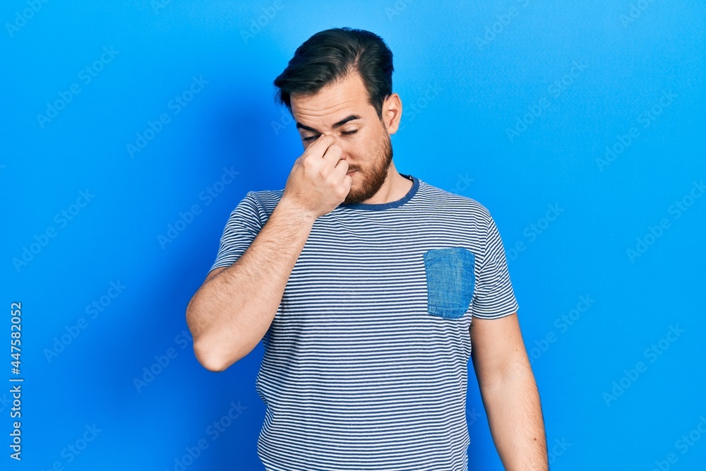 Handsome caucasian man with beard wearing casual striped t shirt tired rubbing nose and eyes feeling fatigue and headache. stress and frustration concept. Handsome caucasian man with beard wearing casual striped t shirt tired rubbing nose and eyes feeling fatigue and headache. stress and frustration concept.