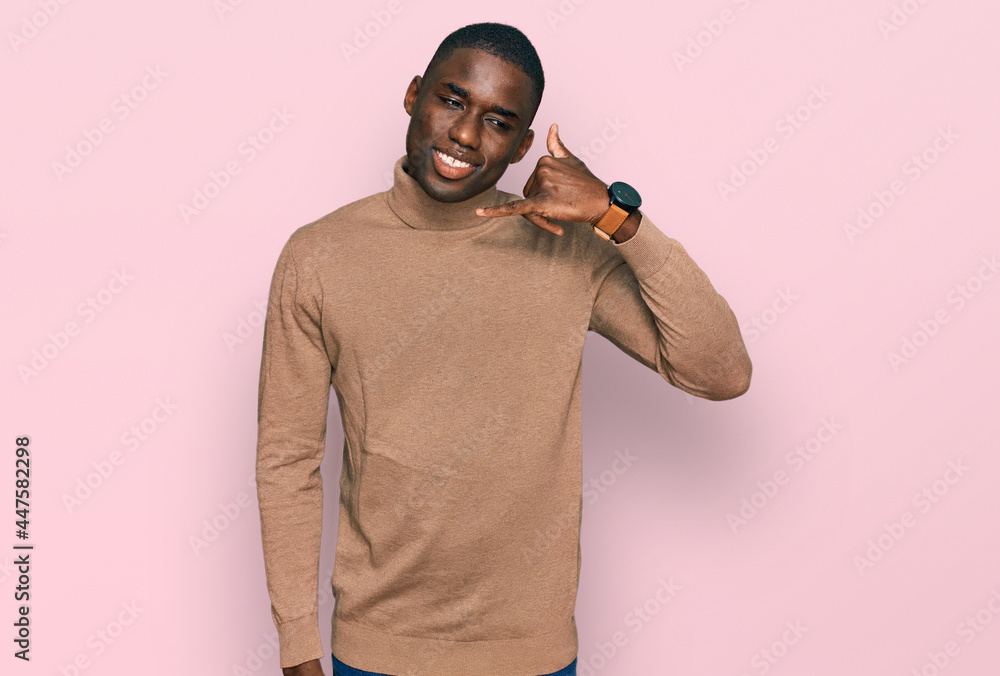Young african american man wearing casual winter sweater smiling doing phone gesture with hand and fingers like talking on the telephone. communicating concepts. Young african american man wearing casual winter sweater smiling doing phone gesture with hand and fingers like talking on the telephone. communicating concepts.