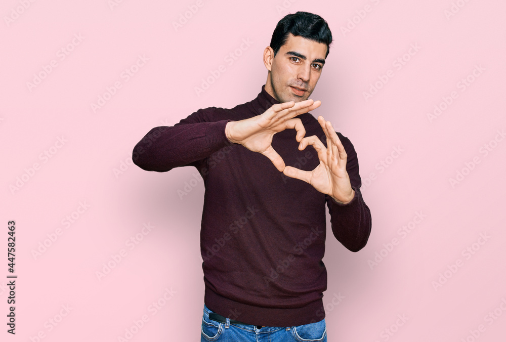 Handsome hispanic man wearing casual turtleneck sweater smiling in love doing heart symbol shape with hands. romantic concept. Handsome hispanic man wearing casual turtleneck sweater smiling in love doing heart symbol shape with hands. romantic concept.