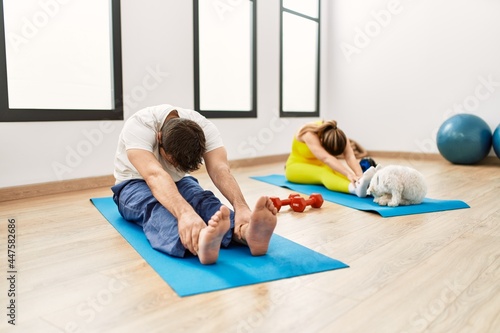 Young hispanic sporty couple stretching sitting on yoga mat at sport center.