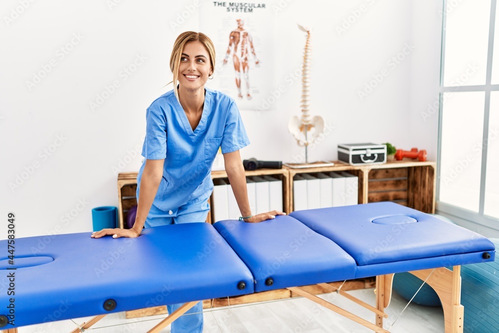 Young caucasian physio therapist smiling happy leaning on table at the clinic Young caucasian physio therapist smiling happy leaning on table at the clinic