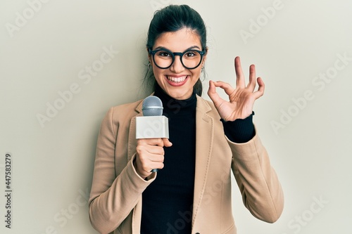 Wallpaper Mural Young hispanic woman holding reporter microphone doing ok sign with fingers, smiling friendly gesturing excellent symbol Torontodigital.ca