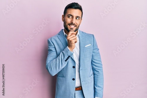 Young hispanic businessman wearing business jacket with hand on chin thinking about question, pensive expression. smiling with thoughtful face. doubt concept.