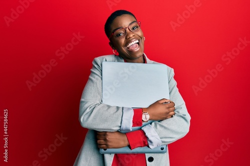 Young african american businesswoman holding laptop winking looking at the camera with sexy expression, cheerful and happy face.