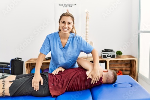 Young hispanic physioterapist woman make back rehab treatment to man at the clinic. photo