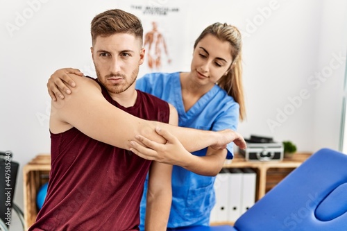 Young hispanic physioterapist woman make arm rehab treatment to man at the clinic.