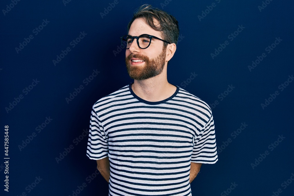 Obraz premium Caucasian man with beard wearing striped t shirt and glasses looking away to side with smile on face, natural expression. laughing confident.