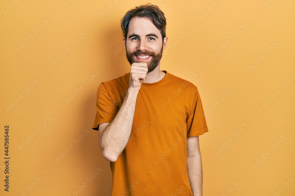 Caucasian man with beard wearing casual yellow t shirt looking confident at the camera smiling with crossed arms and hand raised on chin. thinking positive. Caucasian man with beard wearing casual yellow t shirt looking confident at the camera smiling with crossed arms and hand raised on chin. thinking positive.