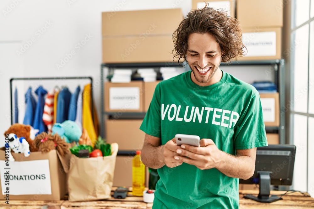 Young hispanic volunteer man smiling happy using smartphone at charity center. Young hispanic volunteer man smiling happy using smartphone at charity center.