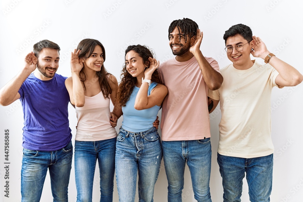 Group of young people standing together over isolated background smiling with hand over ear listening an hearing to rumor or gossip. deafness concept. Group of young people standing together over isolated background smiling with hand over ear listening an hearing to rumor or gossip. deafness concept.