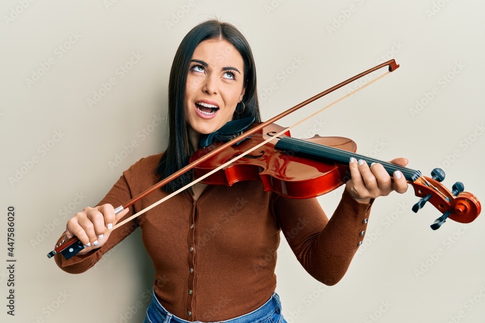 Young brunette woman playing violin angry and mad screaming frustrated and furious, shouting with anger looking up. Young brunette woman playing violin angry and mad screaming frustrated and furious, shouting with anger looking up.