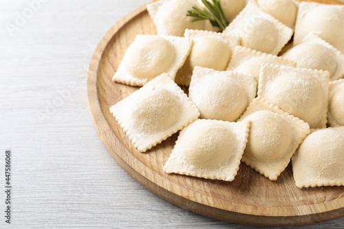 Uncooked ravioli and rosemary on white wooden table, closeup