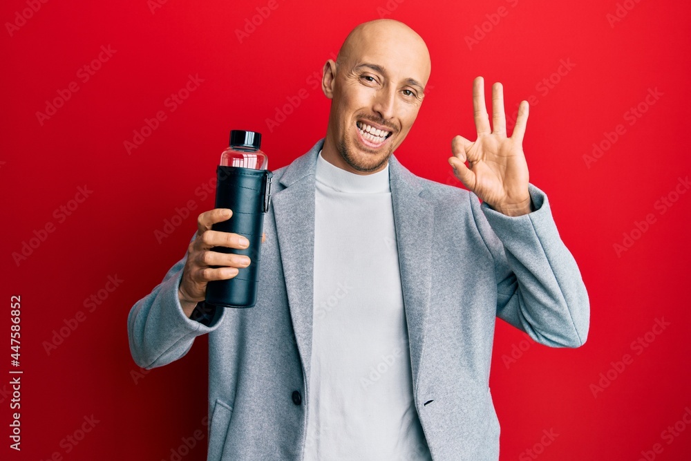 Bald business man with beard drinking bottle of water doing ok sign with fingers, smiling friendly gesturing excellent symbol Bald business man with beard drinking bottle of water doing ok sign with fingers, smiling friendly gesturing excellent symbol