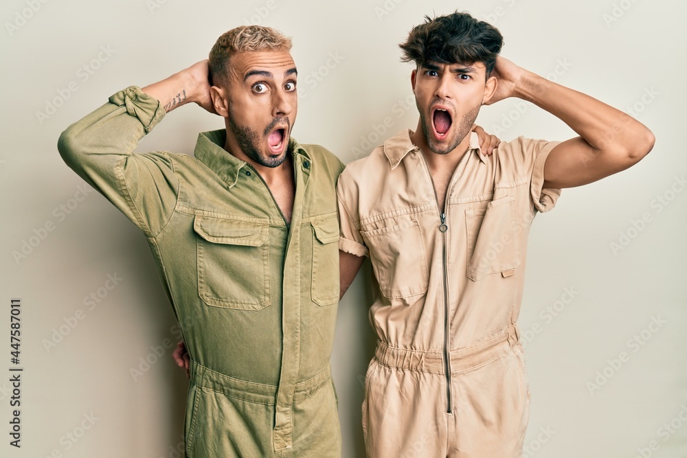 Homosexual gay couple standing together wearing casual jumpsuit crazy and scared with hands on head, afraid and surprised of shock with open mouth Homosexual gay couple standing together wearing casual jumpsuit crazy and scared with hands on head, afraid and surprised of shock with open mouth
