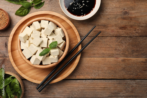 Delicious tofu with basil served on wooden table, flat lay. Space for text