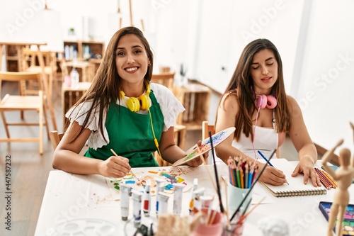 Two latin paint students smiling happy painting sitting on the table at art school.