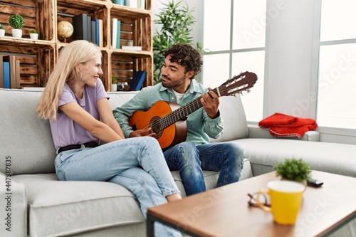 Man playing spanish guitar to his girlfriend sitting on the sofa at home