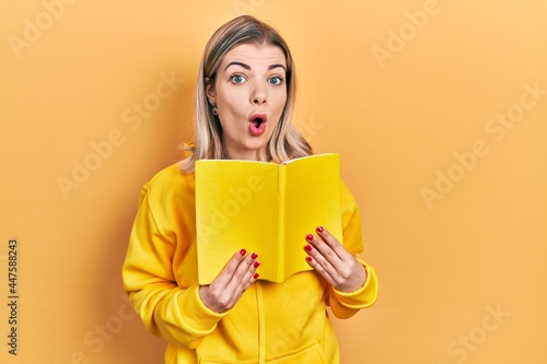 Beautiful caucasian woman holding open book afraid and shocked with surprise and amazed expression, fear and excited face.