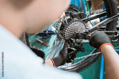 bicycle mechanic's hand with gloves uses an allen key to install the rear derailleur while working in a workshop photo