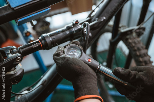 close up of a bicycle mechanic's hand in gloves using a pressure gauge pump to adjust the suspension while repairing a bicycle in a workshop