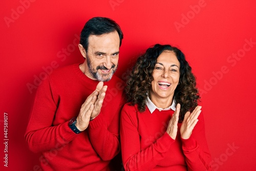Middle age couple of hispanic woman and man hugging and standing together clapping and applauding happy and joyful, smiling proud hands together © Krakenimages.com