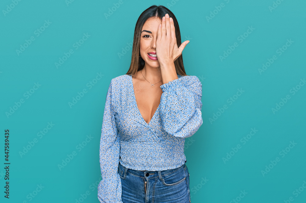 Young hispanic woman wearing casual clothes covering one eye with hand, confident smile on face and surprise emotion. Young hispanic woman wearing casual clothes covering one eye with hand, confident smile on face and surprise emotion.