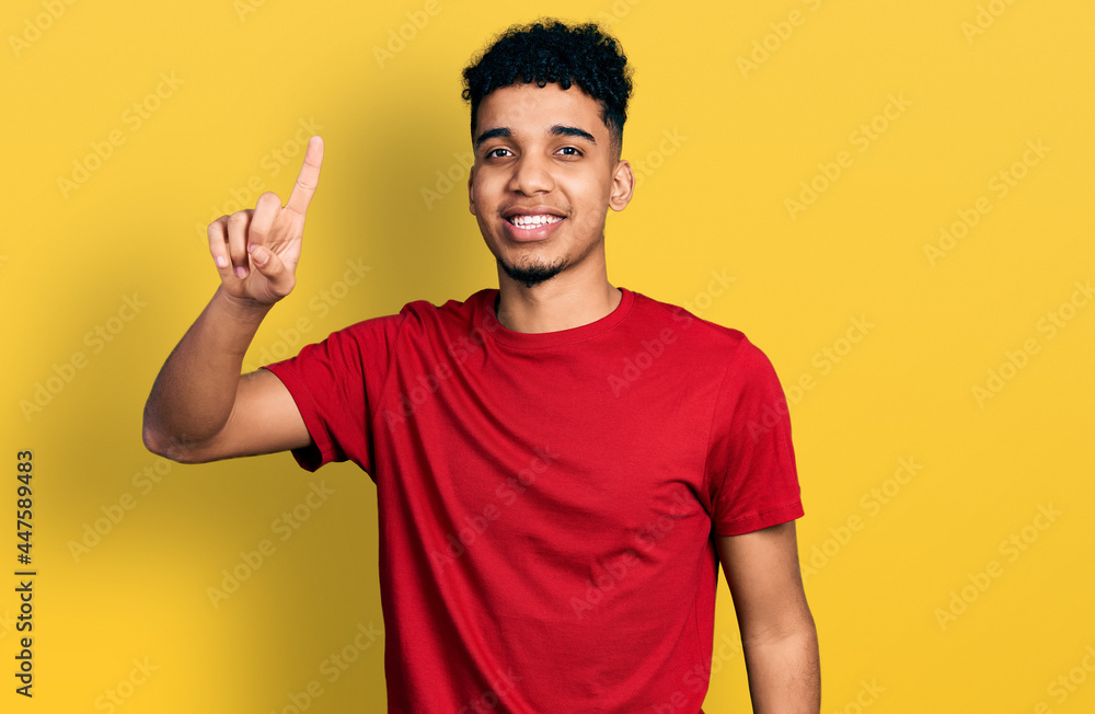 Young african american man wearing casual red t shirt showing and pointing up with finger number one while smiling confident and happy. Young african american man wearing casual red t shirt showing and pointing up with finger number one while smiling confident and happy.