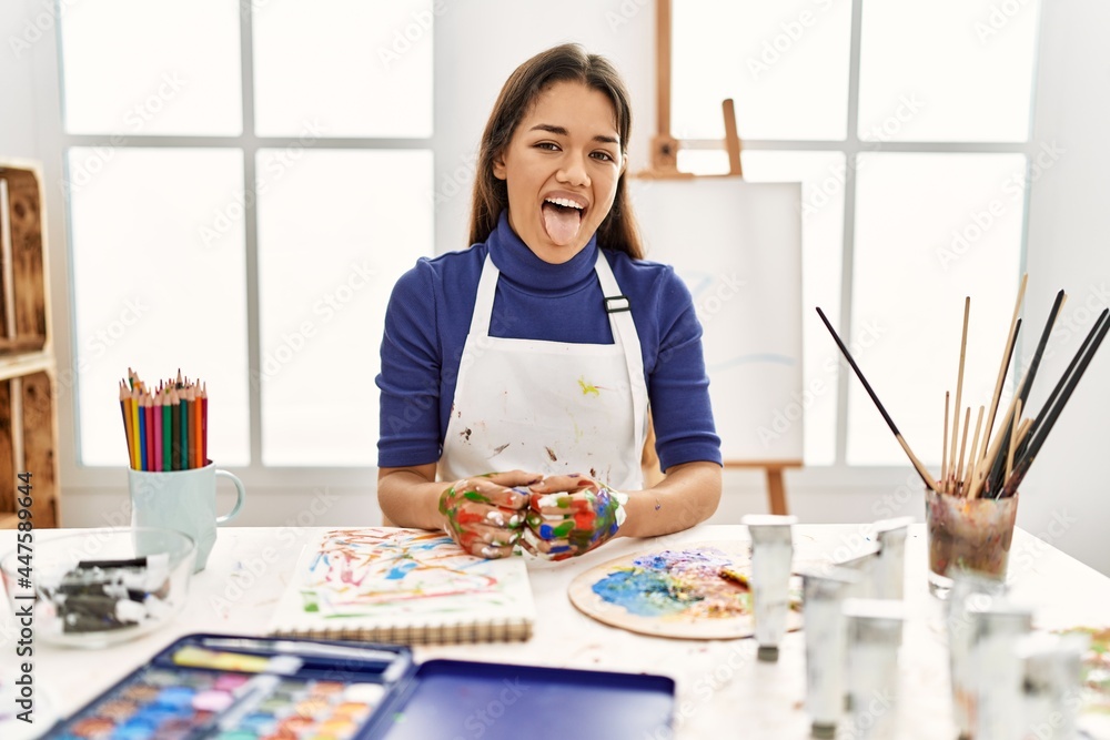 Young brunette woman at art studio with painted hands sticking tongue out happy with funny expression. emotion concept. Young brunette woman at art studio with painted hands sticking tongue out happy with funny expression. emotion concept.
