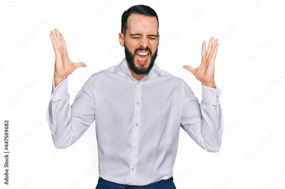 Young man with beard wearing business shirt celebrating mad and crazy for success with arms raised and closed eyes screaming excited. winner concept Young man with beard wearing business shirt celebrating mad and crazy for success with arms raised and closed eyes screaming excited. winner concept