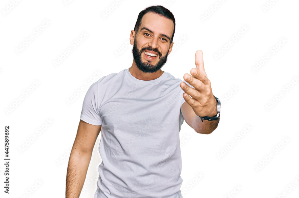 Young man with beard wearing casual white t shirt smiling friendly offering handshake as greeting and welcoming. successful business. Young man with beard wearing casual white t shirt smiling friendly offering handshake as greeting and welcoming. successful business.