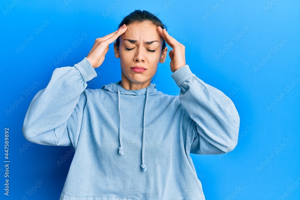 Young caucasian blonde woman wearing casual sweatshirt with hand on head, headache because stress. suffering migraine. Young caucasian blonde woman wearing casual sweatshirt with hand on head, headache because stress. suffering migraine.