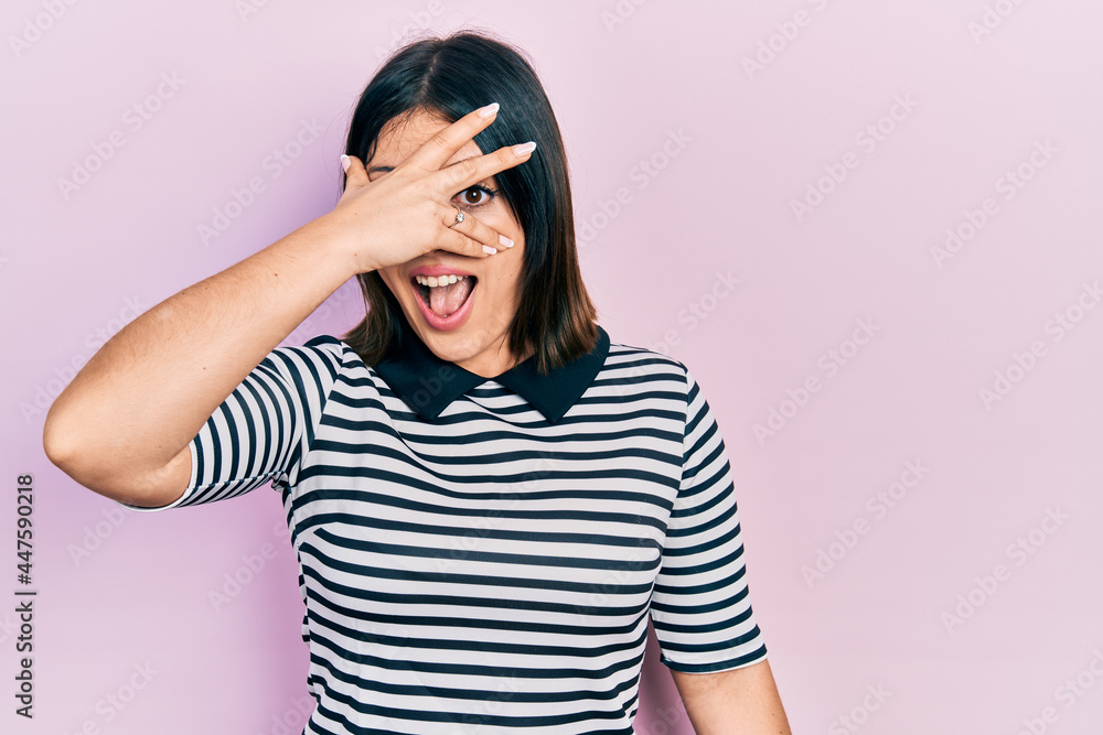 Young hispanic woman wearing casual clothes peeking in shock covering face and eyes with hand, looking through fingers with embarrassed expression. Young hispanic woman wearing casual clothes peeking in shock covering face and eyes with hand, looking through fingers with embarrassed expression.