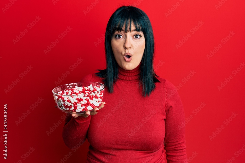 Young hispanic woman holding bowl of pills scared and amazed with open mouth for surprise, disbelief face Young hispanic woman holding bowl of pills scared and amazed with open mouth for surprise, disbelief face