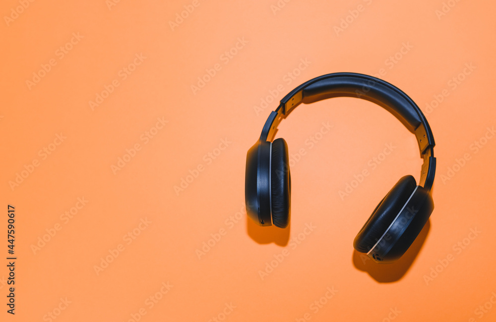 Black wireless headphones isolated on an orange background. Black wireless headphones isolated on an orange background.